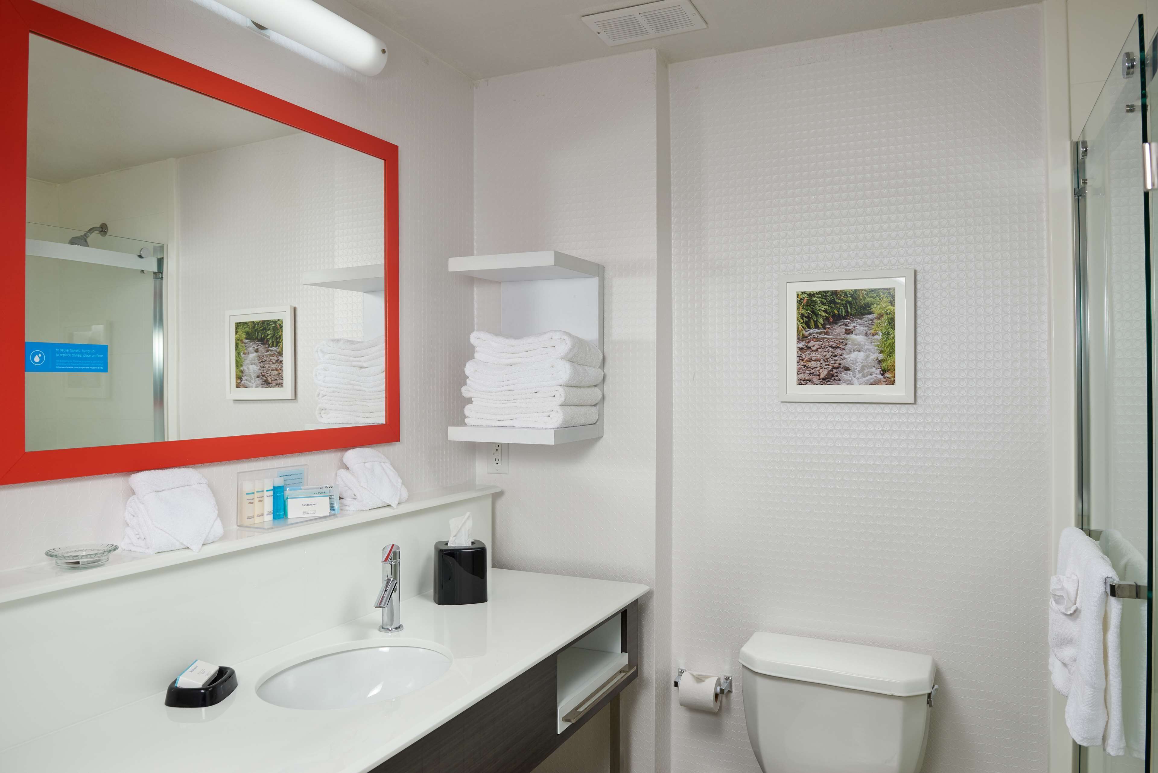 Une salle de bain moderne avec un lavabo blanc, un miroir à cadre rouge, des toilettes et une douche en verre.