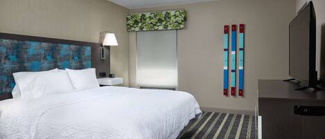 Een hotelkamer met een groot bed, een flatscreen televisie, een bureau en een spiegel.