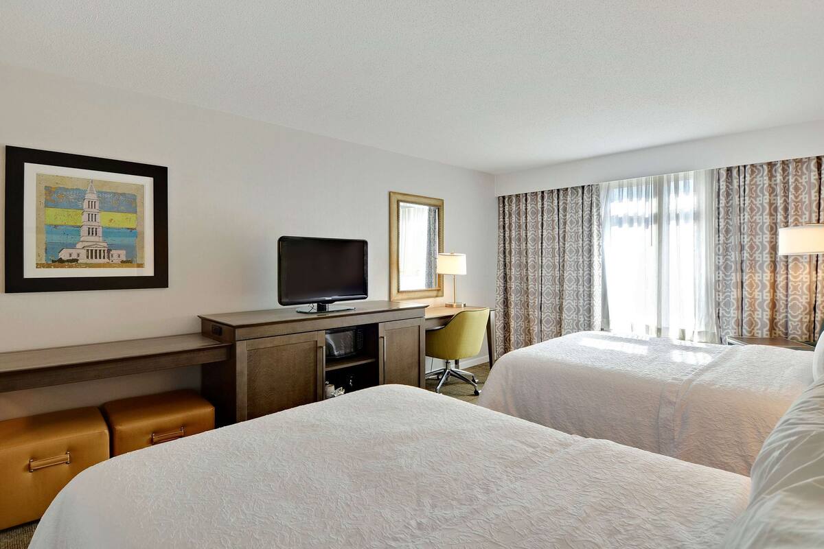 A hotel room with two beds, a desk with a television, a chair, and a framed picture on the wall.