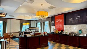 A hotel breakfast area with a check-in counter, seating, and a view of the city. - Hampton Inn Alexandria-Old Town/King St. Metro (Alexandria)