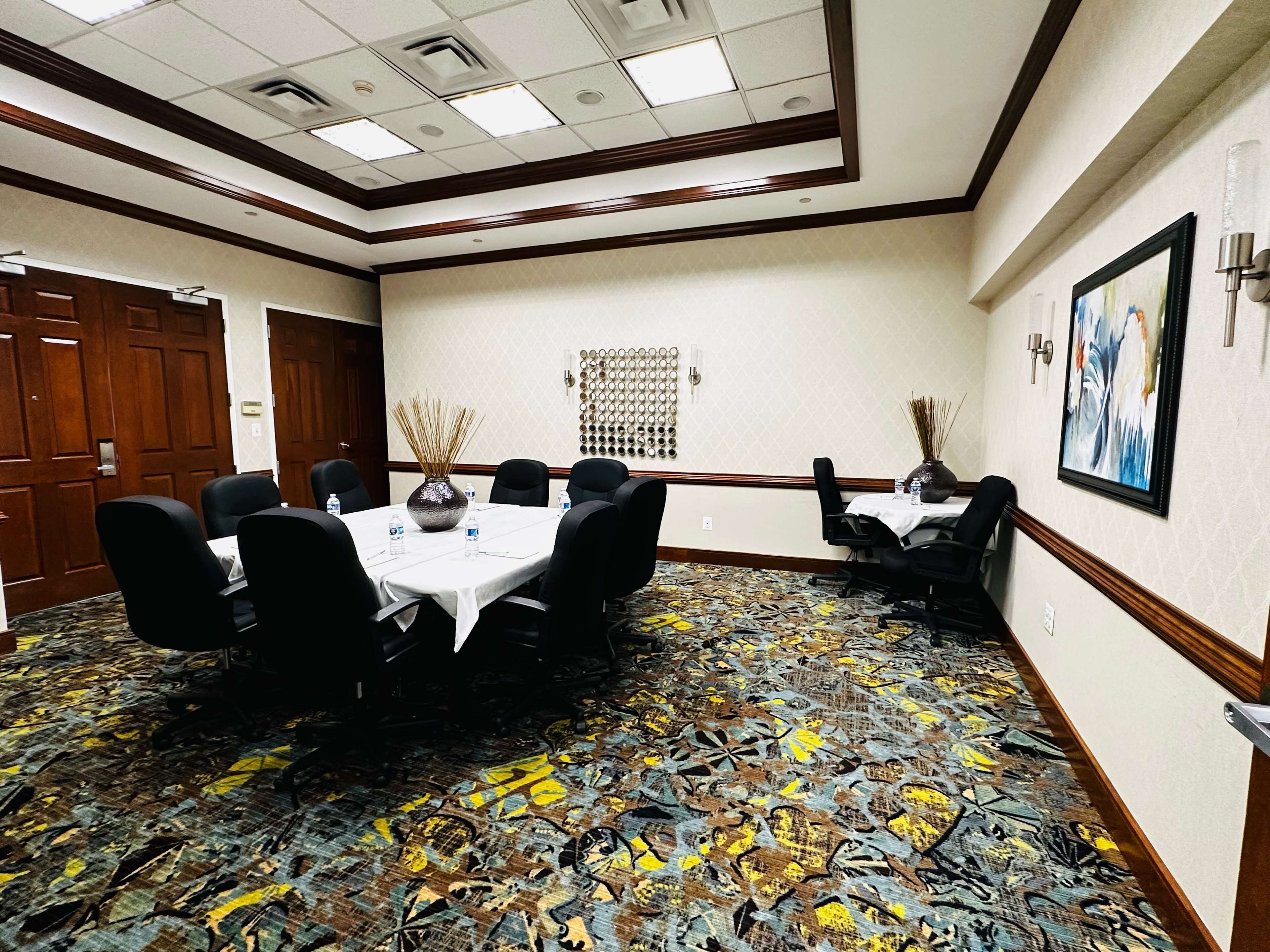 A conference room with a round table, black chairs, and a patterned carpet.