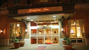 A Hampton Inn hotel entrance with a brick facade, large potted plants, and a neon sign. - Hampton Inn Alexandria-Old Town/King St. Metro (Alexandria)