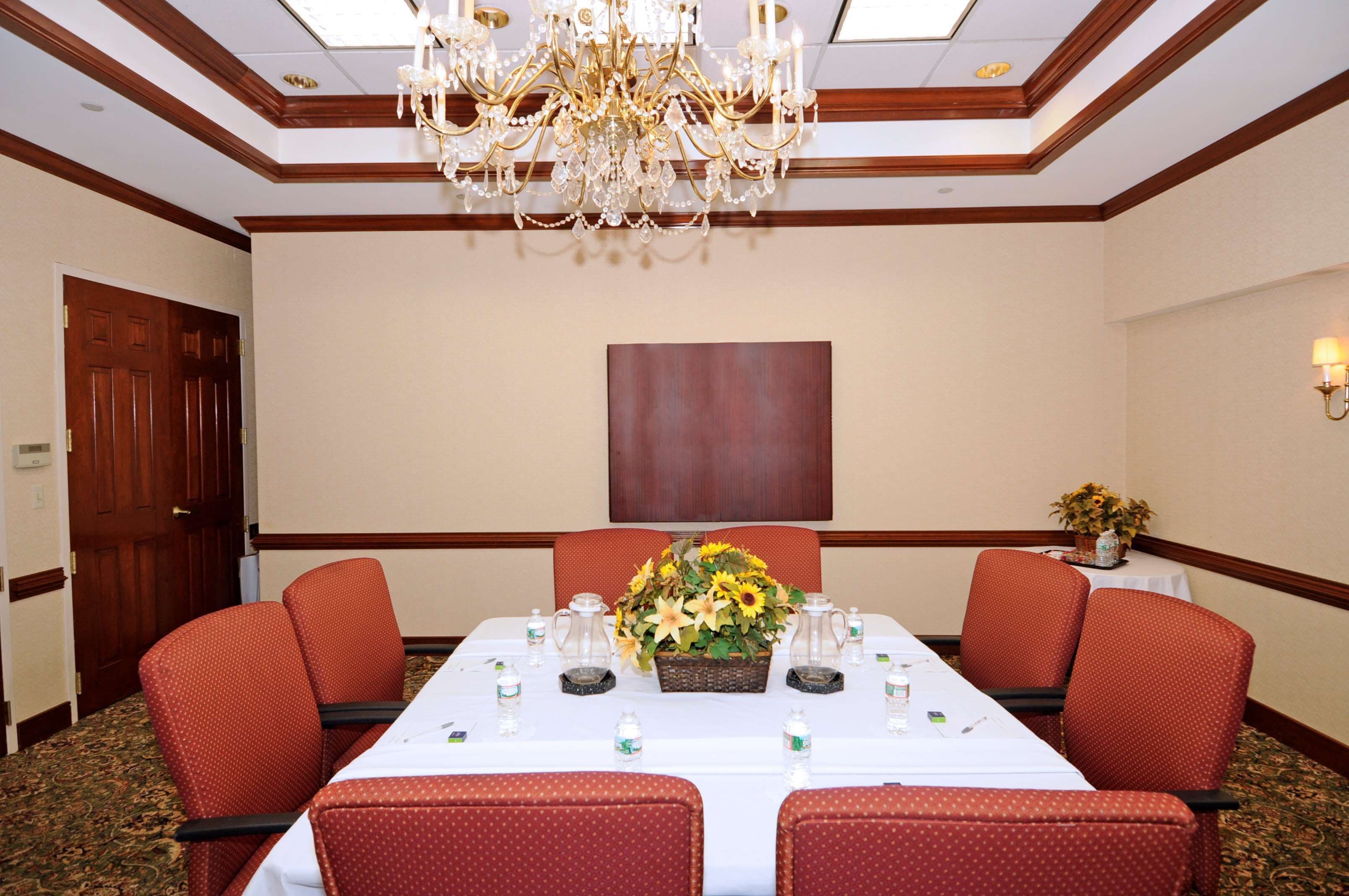 Ein Konferenzraum mit langem Tisch, roten Polsterstühlen, einer Kristallleuchtre und einer Blumendekoration.