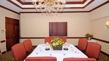 Ein Konferenzraum mit langem Tisch, roten Polsterstühlen, einer Kristallleuchtre und einer Blumendekoration.