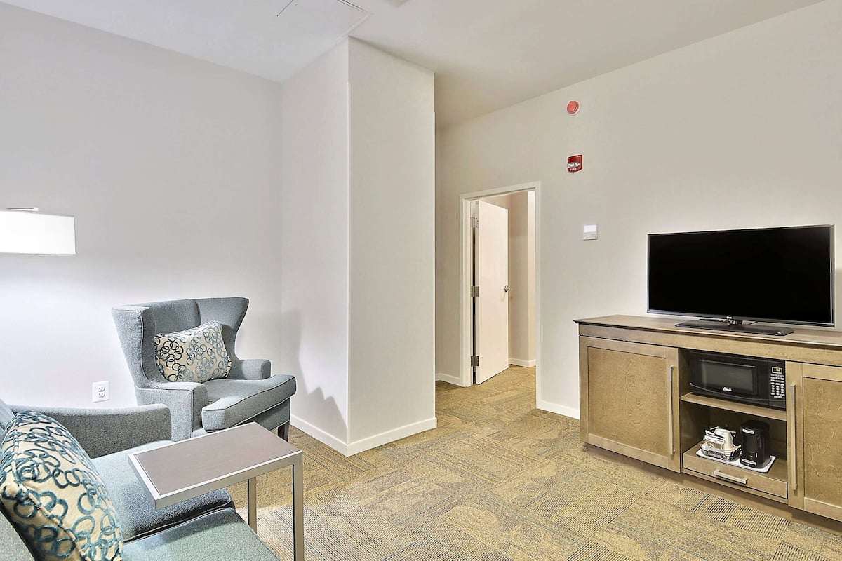 A modern living room with a grey sofa, a small table, a flat-screen TV, and a wooden cabinet with a microwave.