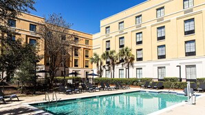 A swimming pool with lounge chairs, a fence, and a building with multiple windows and balconies. - Hampton Inn Charleston - Daniel Island (Charleston)