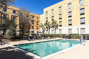 A hotel pool area with lounge chairs and umbrellas, surrounded by a building with multiple windows and balconies. - Hampton Inn Charleston - Daniel Island (Charleston)