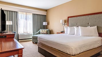 A hotel room with a large bed, a desk, a chair, a TV, a lamp, and a window with curtains.