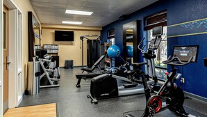 A gym with exercise equipment, a wall-mounted TV, and a window with blinds. - Hampton Inn Charleston - Daniel Island (Charleston)