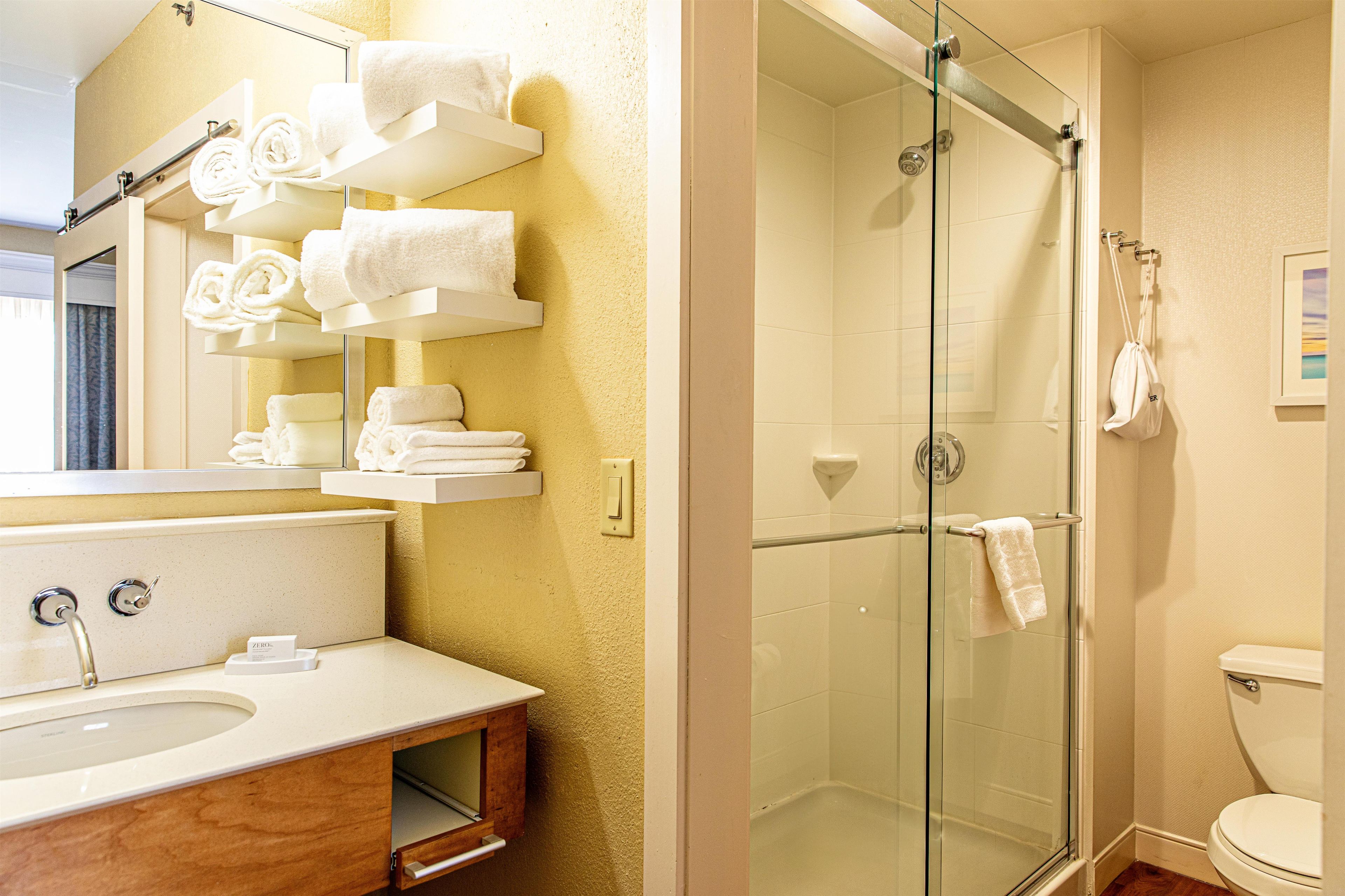 A bathroom with a glass-enclosed shower, a sink, and a mirror with towels.