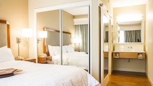 A hotel room with a large bed, a bedside table with a lamp, a mirror, and a wooden floor. - Hampton Inn Charleston - Daniel Island (Charleston)