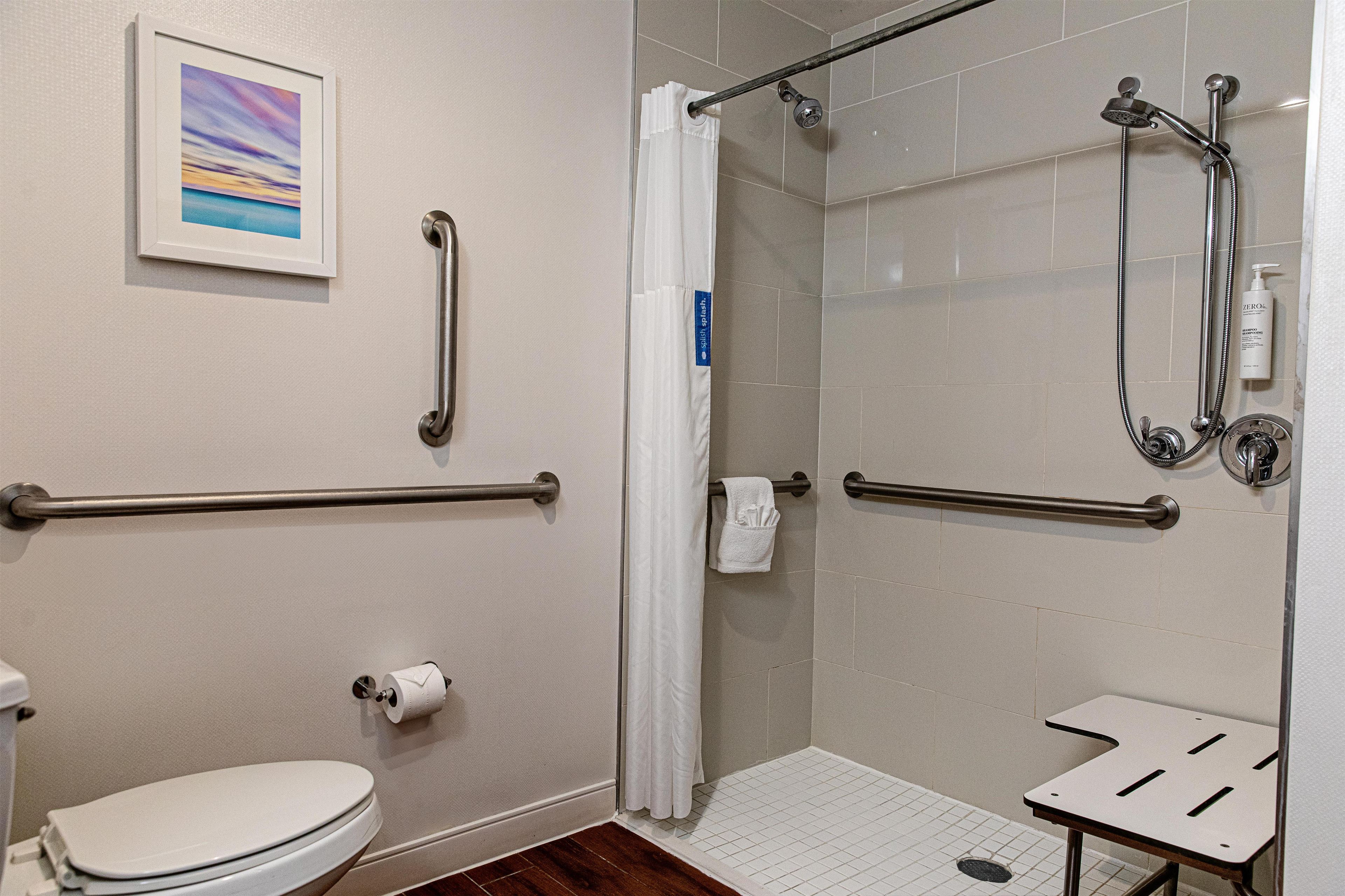 Une salle de bain comprenant des toilettes, une douche avec une porte en verre, une barre d’appui et un porte-serviettes.