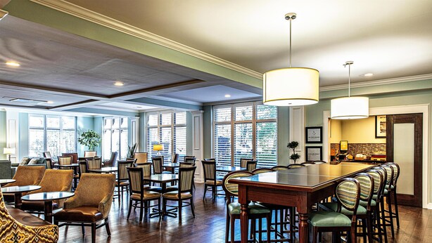 A spacious dining area with high ceilings, large windows, and a long communal table with bar stools. - Hampton Inn Charleston - Daniel Island (Charleston)
