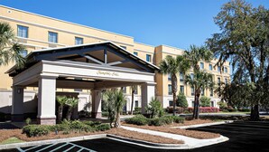 A hotel entrance with a covered area, palm trees, and a clear sky. - Hampton Inn Charleston - Daniel Island (Charleston)