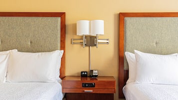A hotel room with two beds, a nightstand with a lamp, a clock, and a drawer.