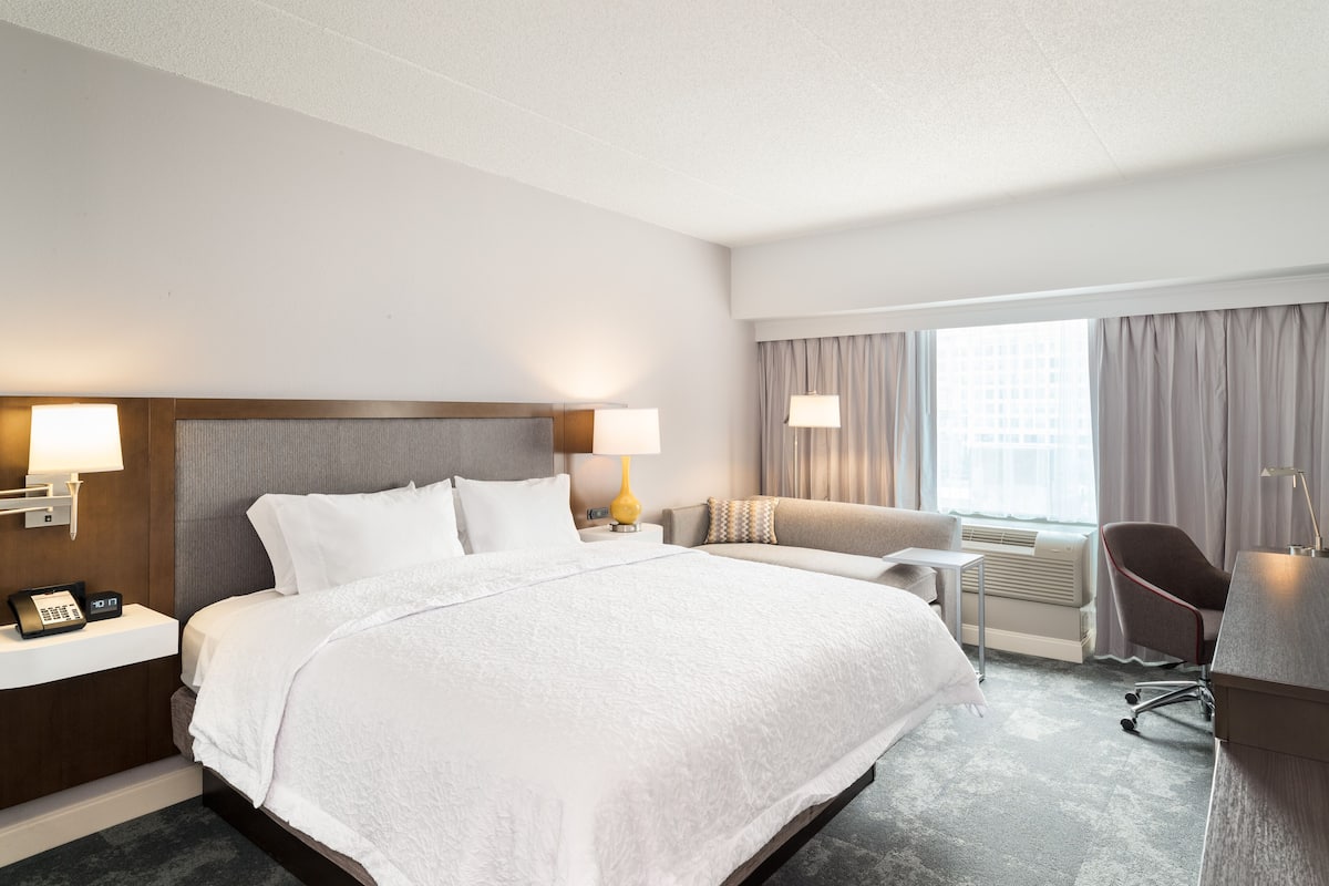 A hotel room with a large bed, bedside lamps, a desk, and a chair.