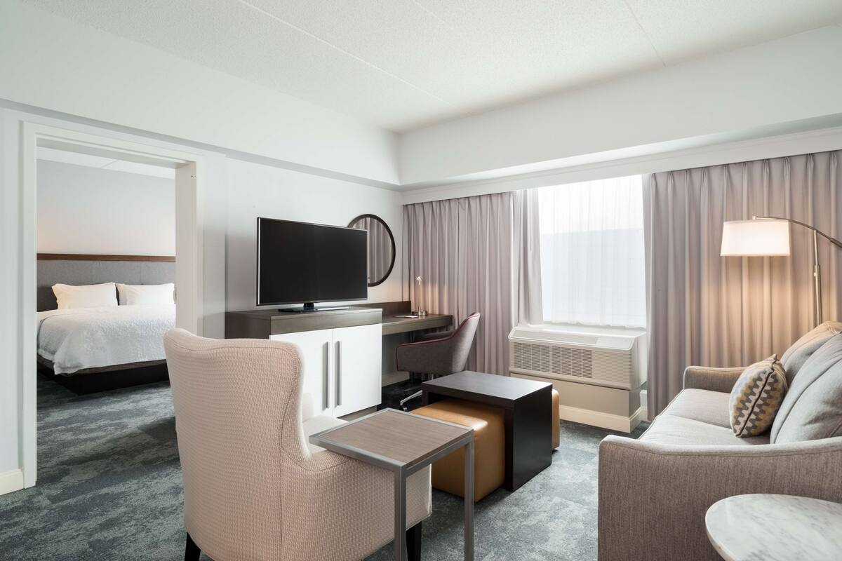 A hotel room with a bed, a desk with a TV, a sofa, a chair, and a lamp.