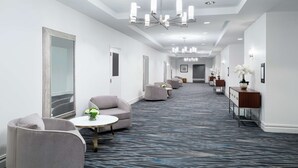 Un pasillo de hotel con zonas de estar, una araña y una alfombra estampada.