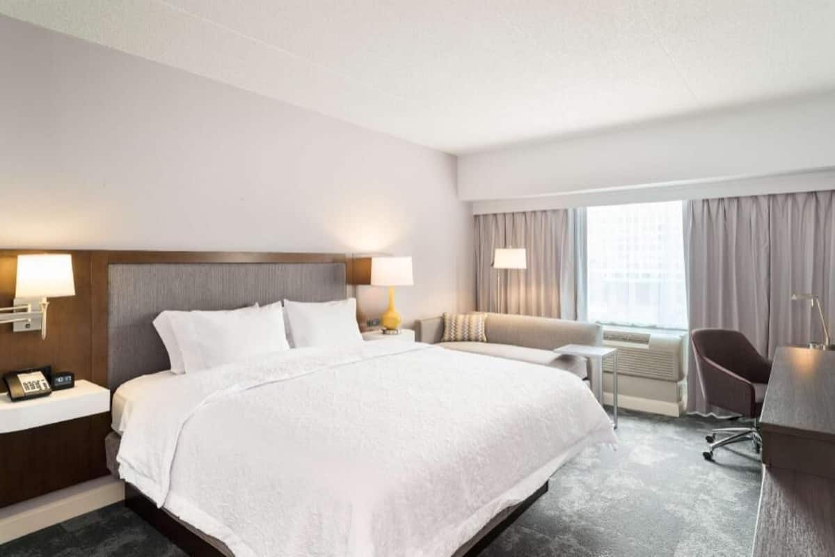 A hotel room with a large bed, bedside tables with lamps, a sofa, a desk, and a chair.