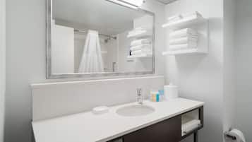 Une salle de bain moderne avec un grand miroir, un lavabo blanc et un espace de rangement pour les serviettes.