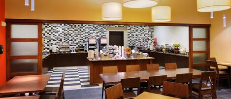 A restaurant with a checkered floor, wooden tables and chairs, and a central counter with various food items and a coffee machine.