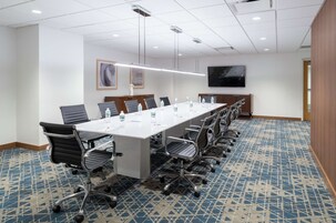 Una sala conferenze con un lungo tavolo, sedie, bottiglie d'acqua e una televisione appesa al muro.