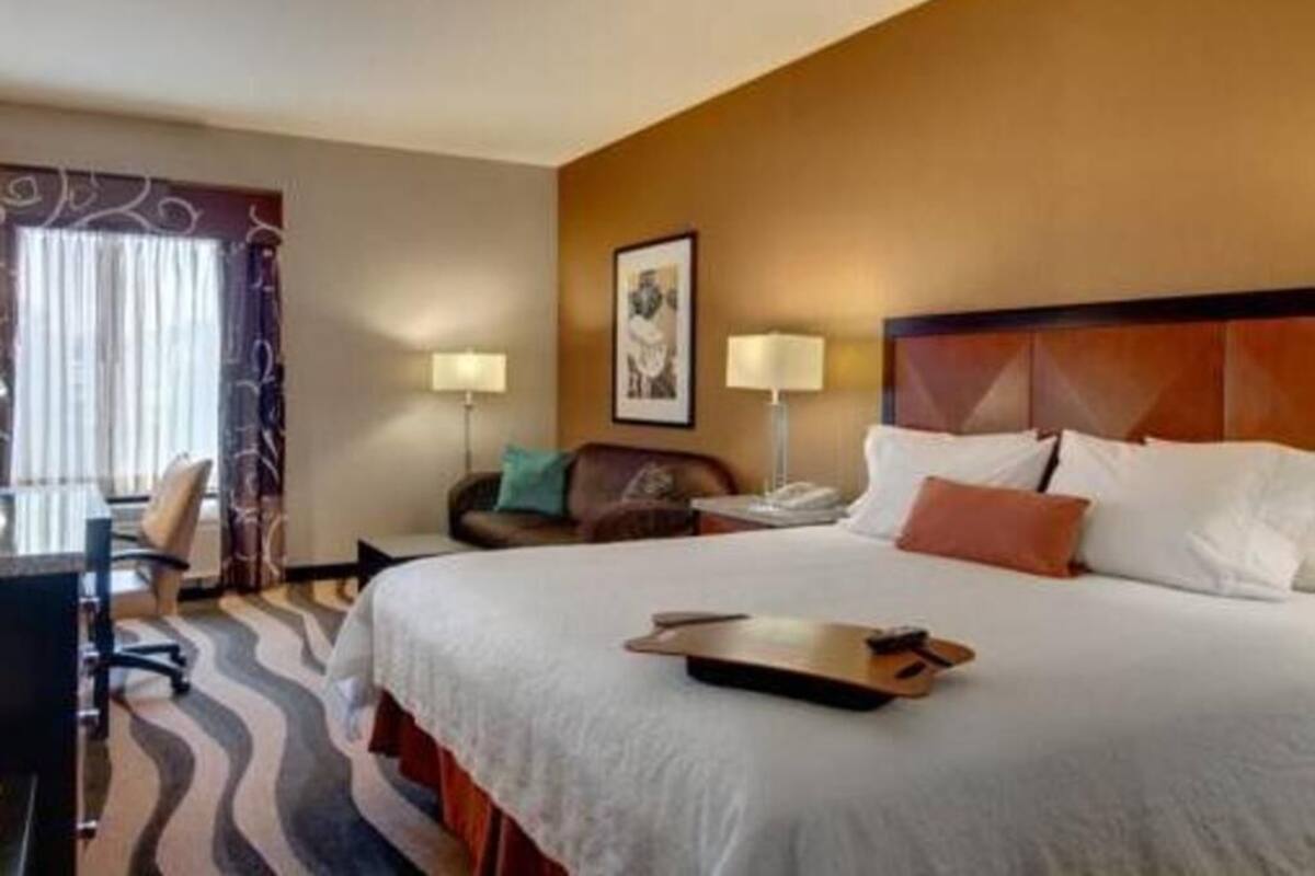 Una habitación de hotel con una cama grande, un escritorio con silla, una lámpara y un cuadro en la pared.