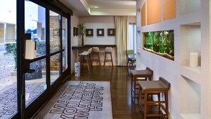 Un hall d’hôtel avec un plancher en bois, un comptoir de réception, un espace salon avec des fauteuils et un grand aquarium mural.