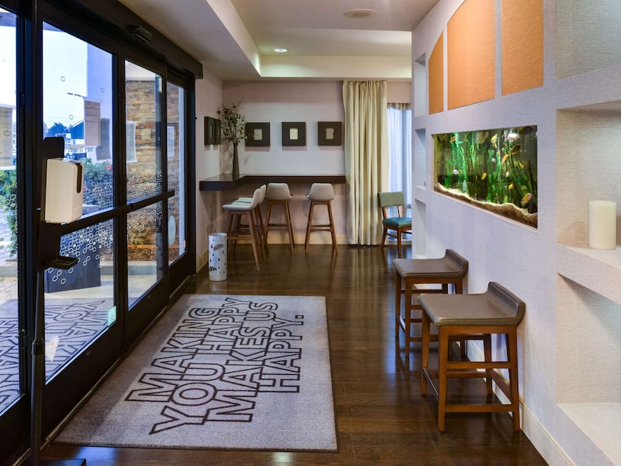 Un hall d’hôtel avec un plancher en bois, un comptoir de réception, un espace salon avec des fauteuils et un grand aquarium mural.