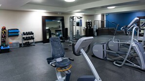 Une salle de sport équipée de matériel d’exercice, dotée d’un mur avec des miroirs et d’un escalier.