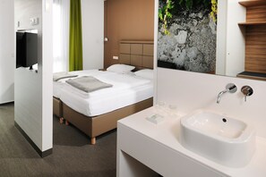 A modern hotel room with a bed, a white bathroom with a sink, and a green curtain. - Hotel INNdependence (Mainz)