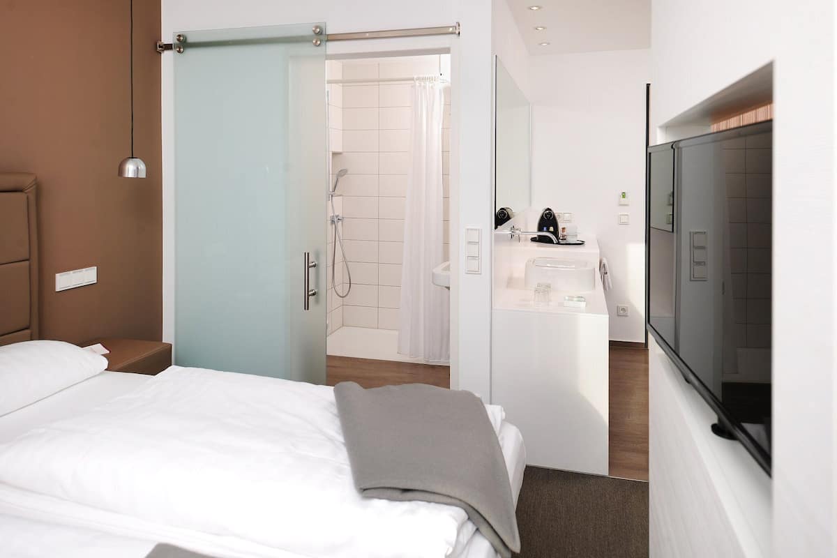 A hotel room with a bed, a bathroom with a shower, a sink, and a TV mounted on the wall.