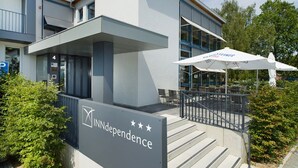 A modern building with a sign reading "INNdependence" and a covered outdoor seating area with umbrellas. - Hotel INNdependence (Mainz)