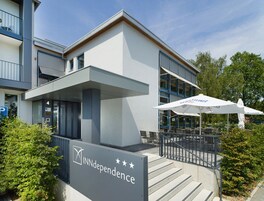 Un edificio moderno con un letrero que dice "INNdependence" y una zona de estar al aire libre cubierta con sombrillas.