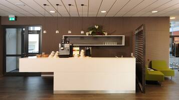 Een receptie met een witte balie, een koffieapparaat en decoratieve planten.