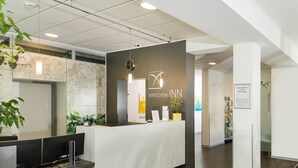 A reception desk with a clock, a welcome sign, and a sign indicating independence. - Hotel INNdependence (Mainz)