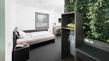 Une chambre d’hôtel moderne équipée d’un lit, d’un bureau, d’une armoire et d’un mur recouvert de plantes vertes.
