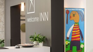 A reception desk with a clock, a welcome sign, and a painting. - Hotel INNdependence (Mainz)