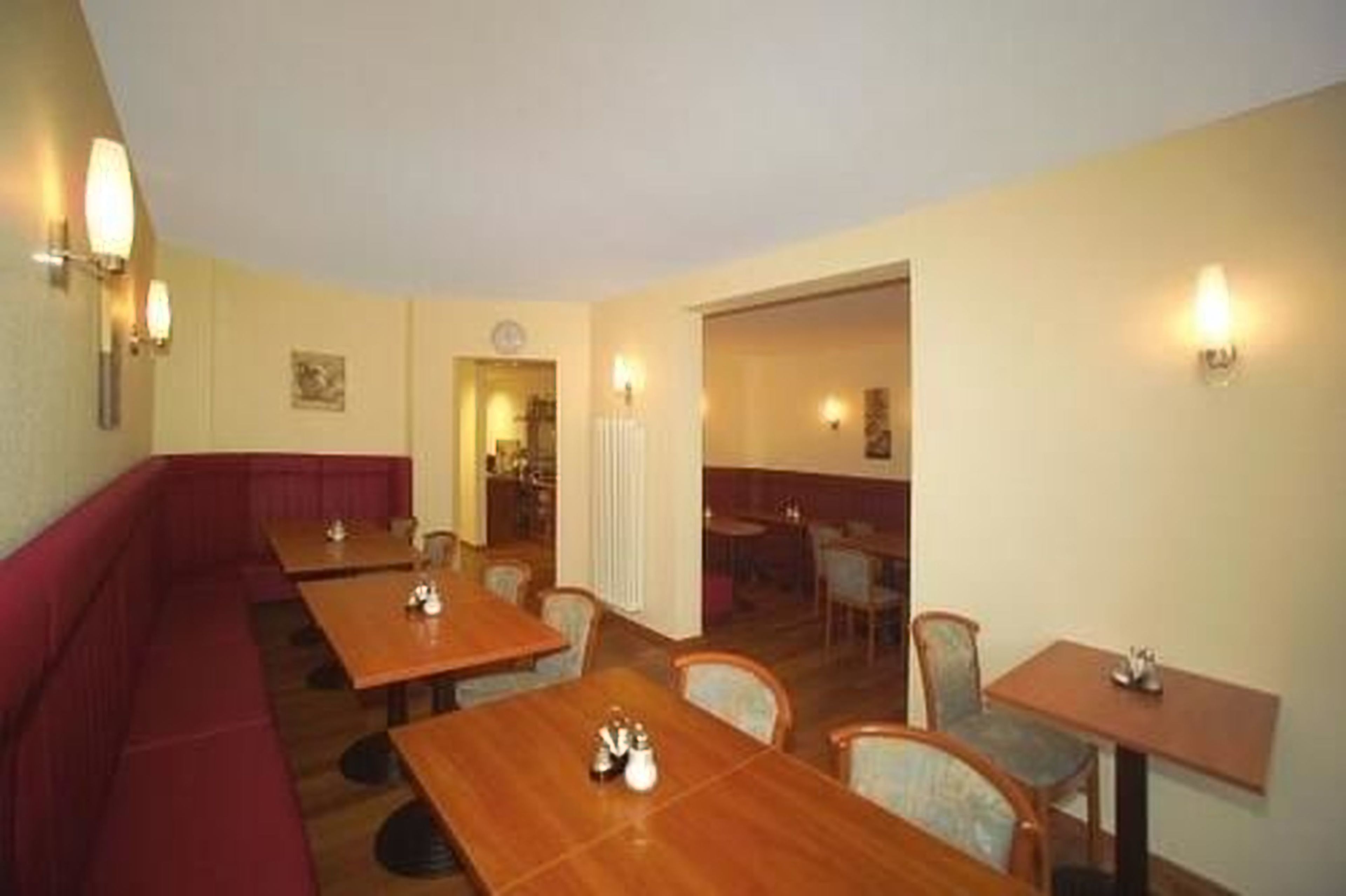 Ein Restaurant mit Sitzgelegenheiten in Form von Boxsitzgruppen und Tischen, einer rot gepolsterten Bank und Wandleuchten.