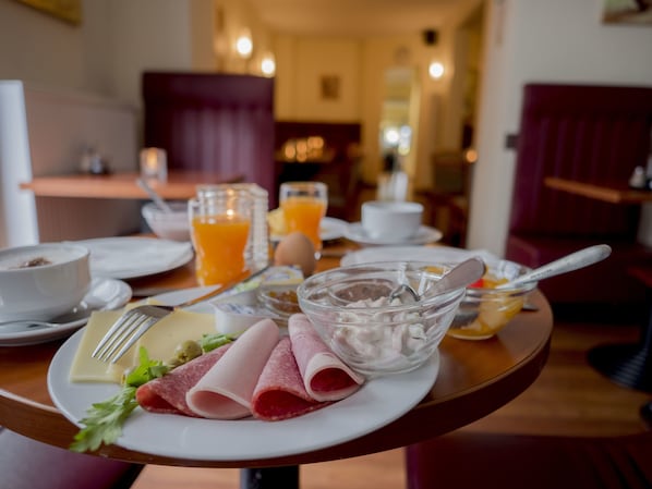 Ein Frühstücksbrett mit Schinken, Käse und einer Schüssel Müsli auf einem Hotel Tisch.