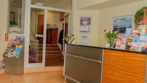 Un espace d’accueil d’hôtel avec un comptoir en bois, une porte vitrée donnant sur un escalier, et divers affiches d’information accrochées au mur.