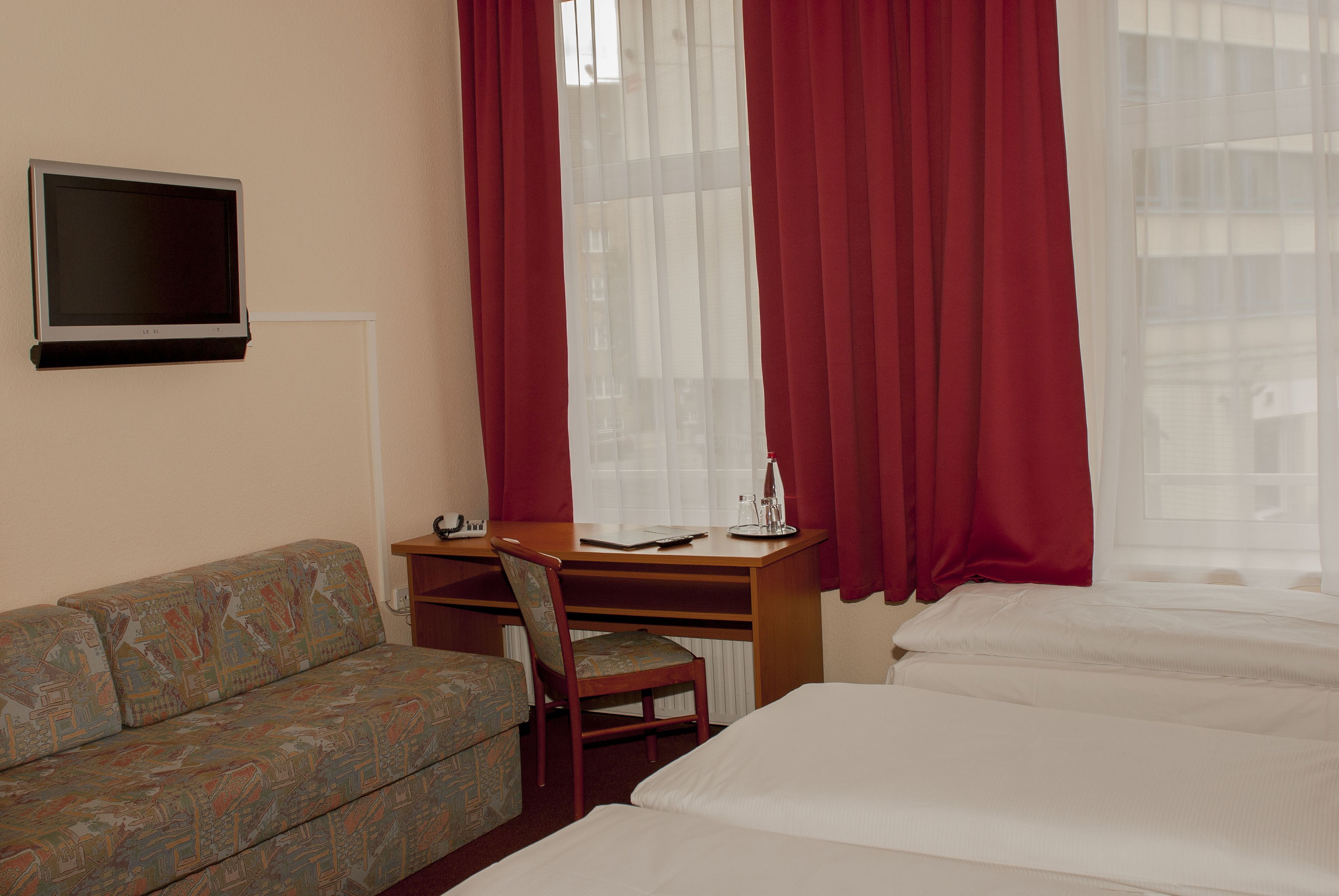 Una habitación de hotel con una cama, un escritorio con una silla, un televisor y un sofá.