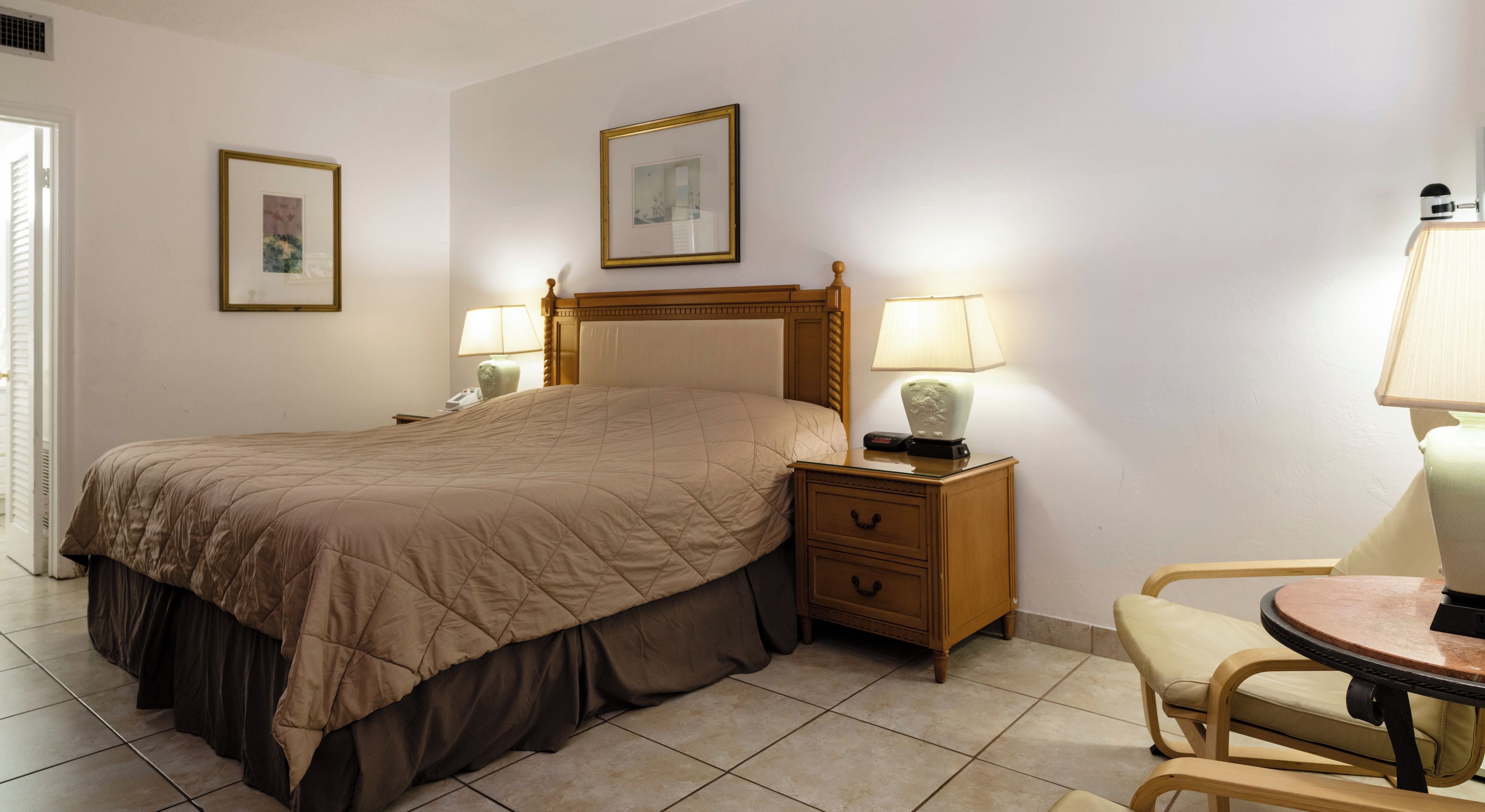 Ein Hotelzimmer mit einem großen Bett, Nachttischen inklusive Lampen, einem Sessel und zwei gerahmten Bildern an der Wand.