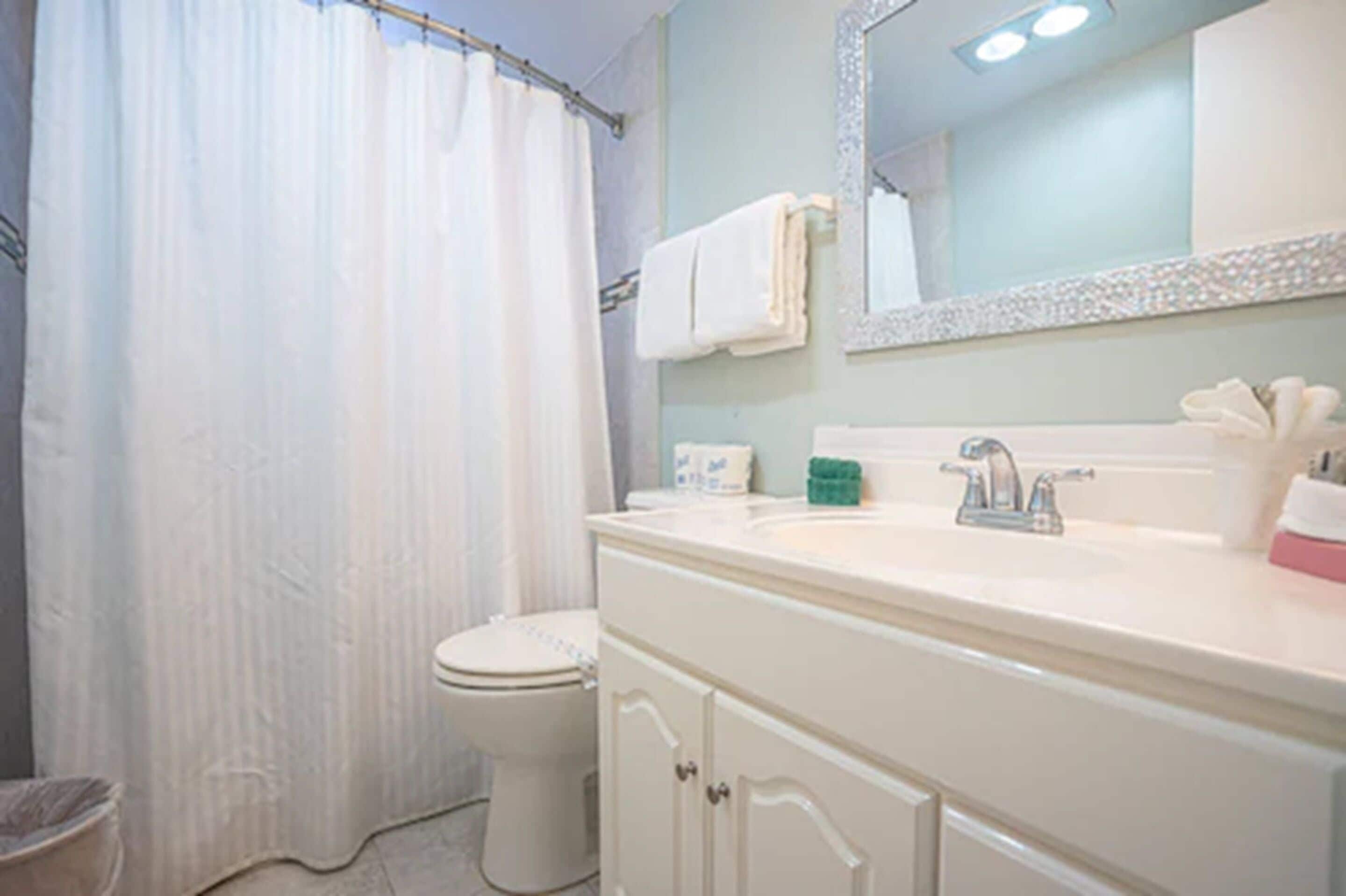 A bathroom with a shower curtain, a toilet, a sink with a mirror, and a cabinet.