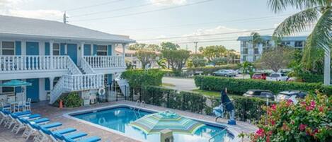 A hotel with a swimming pool, lounge chairs, and a staircase leading to the upper floor.