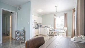 Una cocina moderna con armarios blancos, una mesa de comedor y sillas. Hay una pequeña mesita de madera y un lámpara colgante.