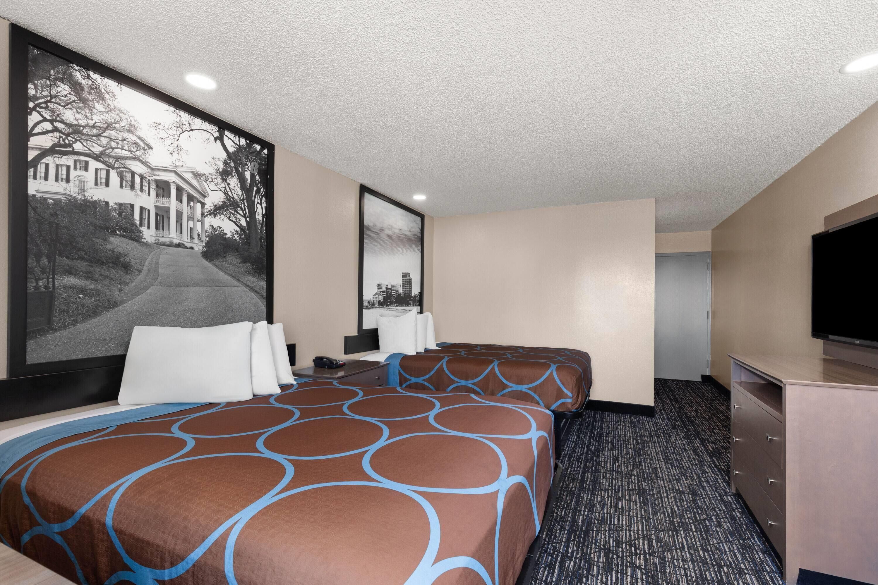 Habitación de hotel con dos camas, un ventanal con vistas a la ciudad, un televisor de pantalla plana y un escritorio con teléfono.
