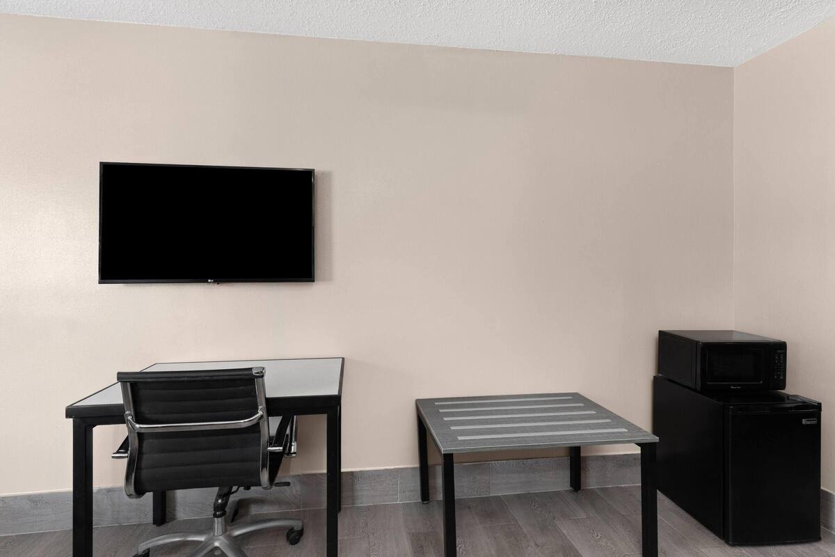 A room with a flat-screen TV mounted on the wall, a black office chair, a small table, and a black refrigerator.