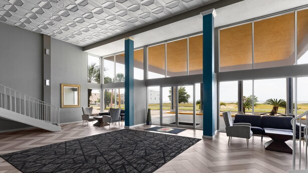 A spacious lobby with a herringbone floor, large windows, and a staircase.