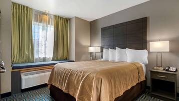 Habitación de hotel con una cama grande, una mesita de noche con lámpara, una ventana con cortinas y un banco empotrado debajo de la ventana.